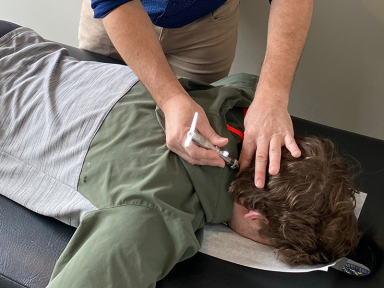 Photo of Dr. Brian Martin using the integrator tool on a patient lying face down on a chiropractic adjustment table at Life Force Chiropractic.